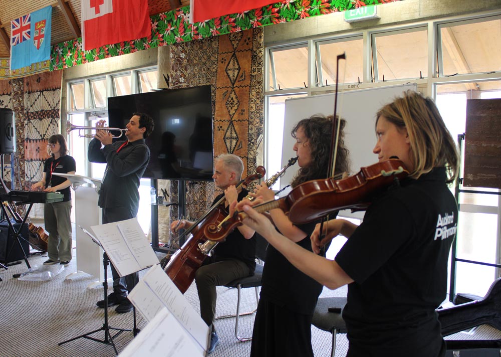 Five musicians perform on keyboards, wind and brass instruments inside a fale at the South Auckland prison